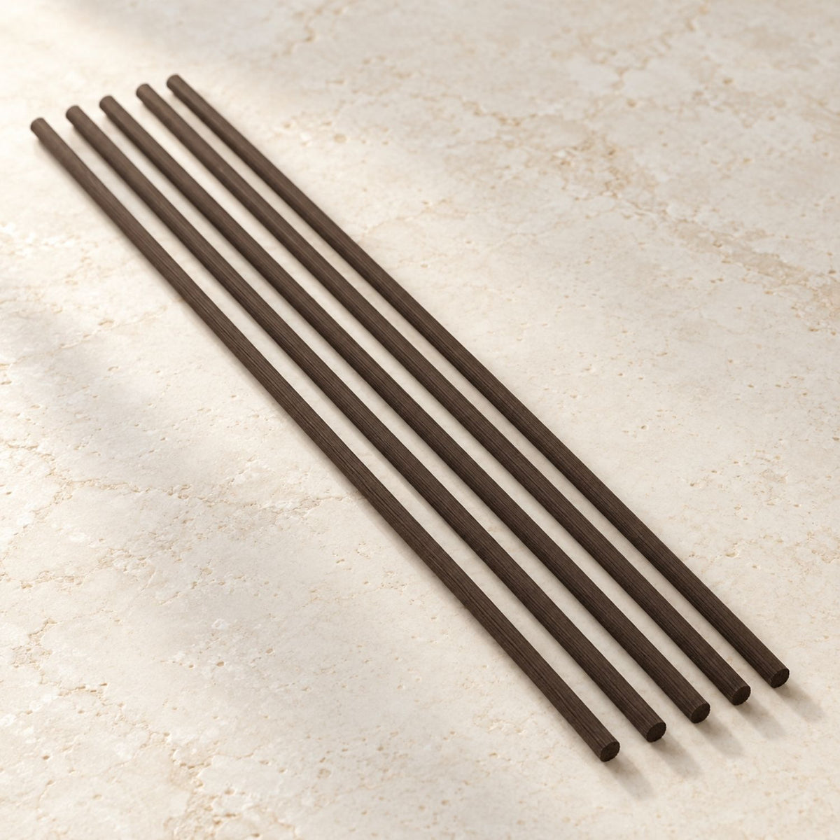 Five Deep Brown Kaze no Shizuku fibre reeds arranged on a warm stone surface
