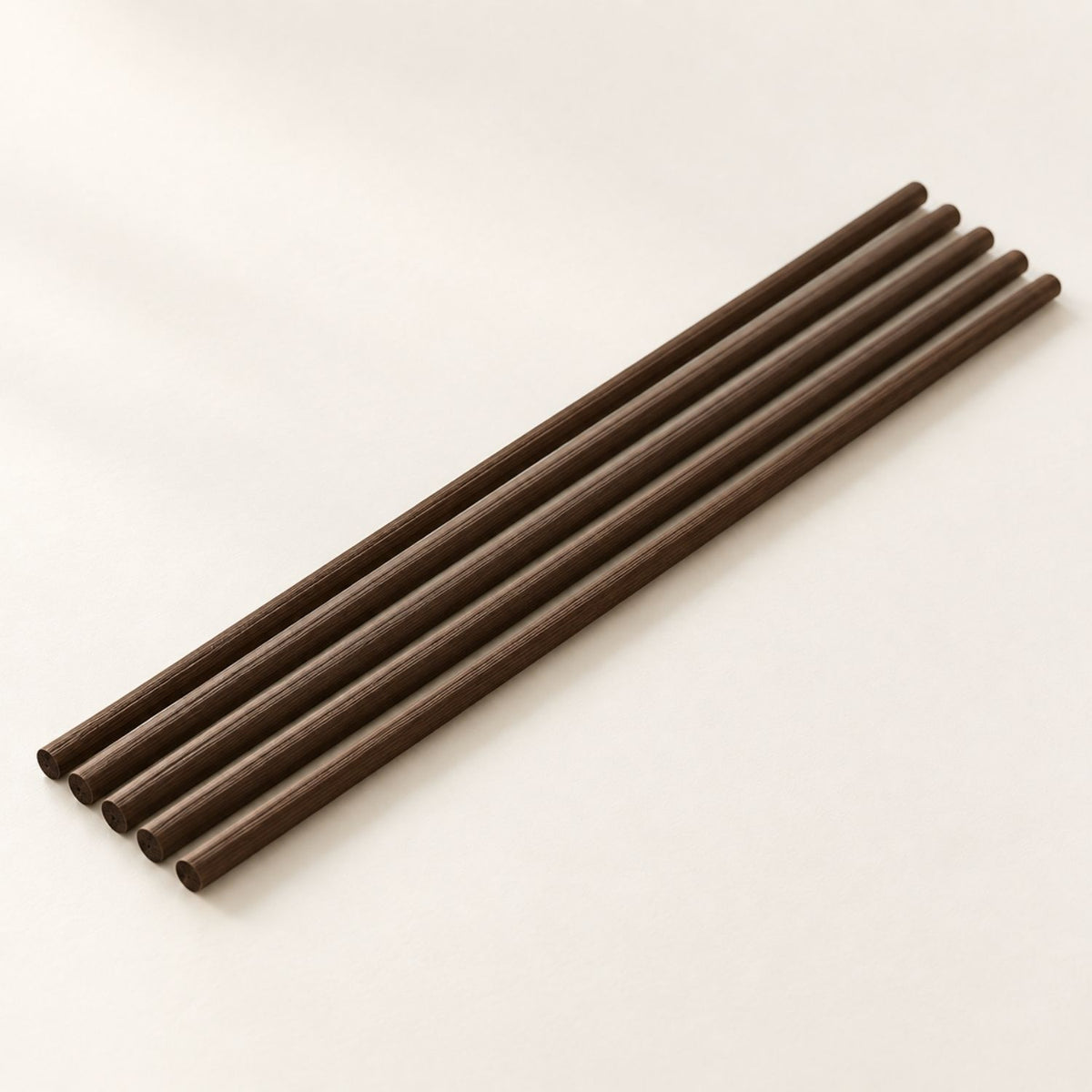 Five Kuro Kaze Deep Brown fibre diffuser reeds arranged diagonally on an ivory